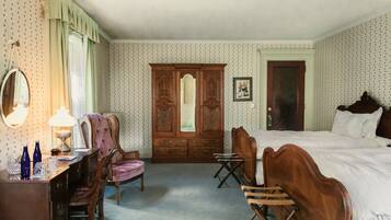 A hotel room with a large wooden wardrobe, a desk with a lamp, a chair, and a bed.