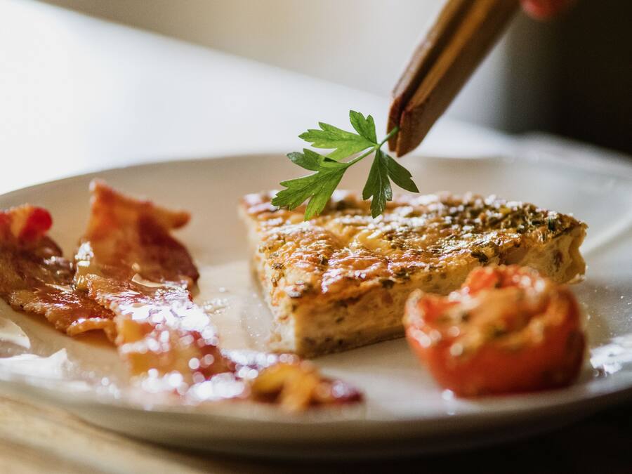 A close-up of a breakfast plate with a piece of toast, bacon, and a tomato.