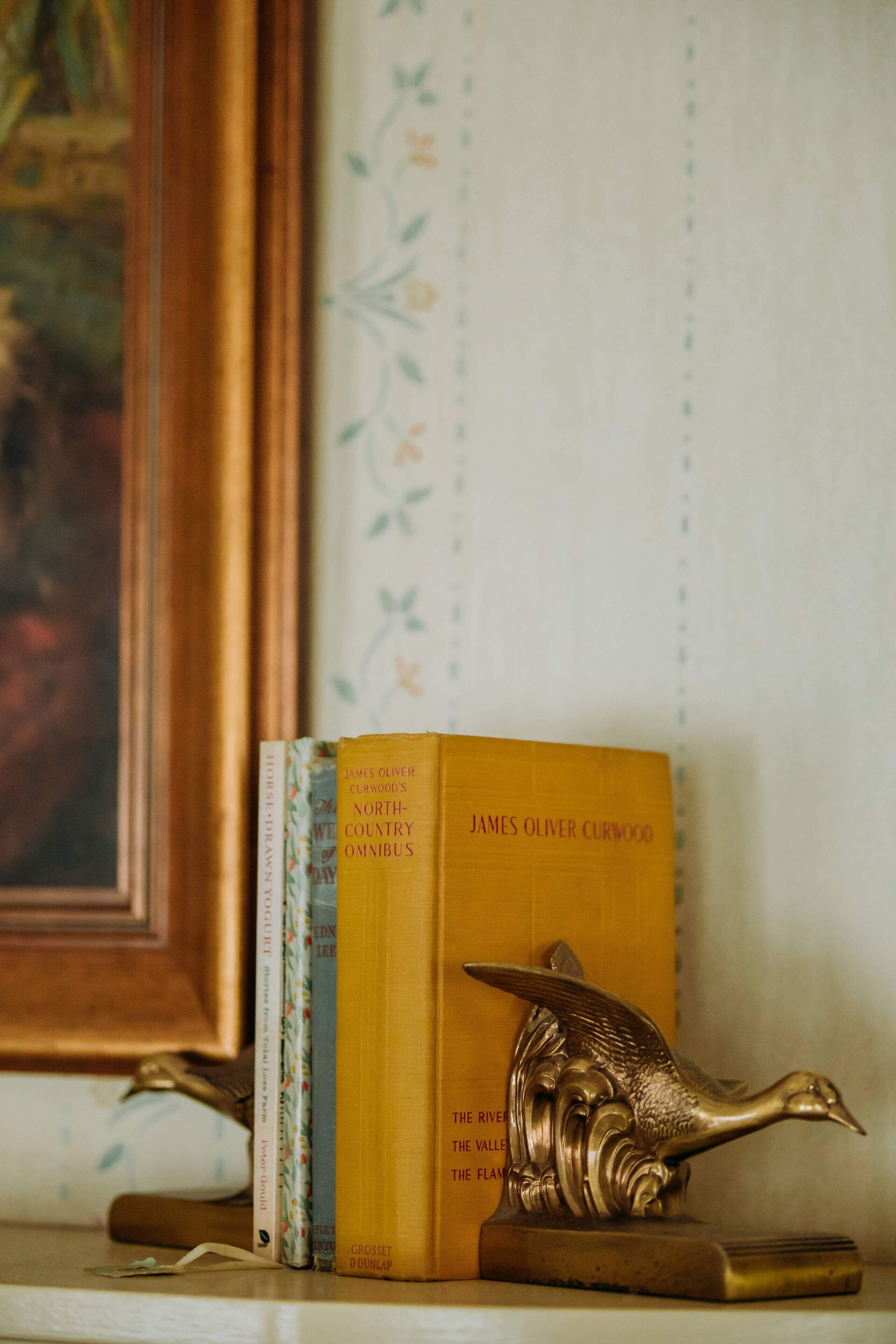 A bookshelf with books and a decorative brass bird.
