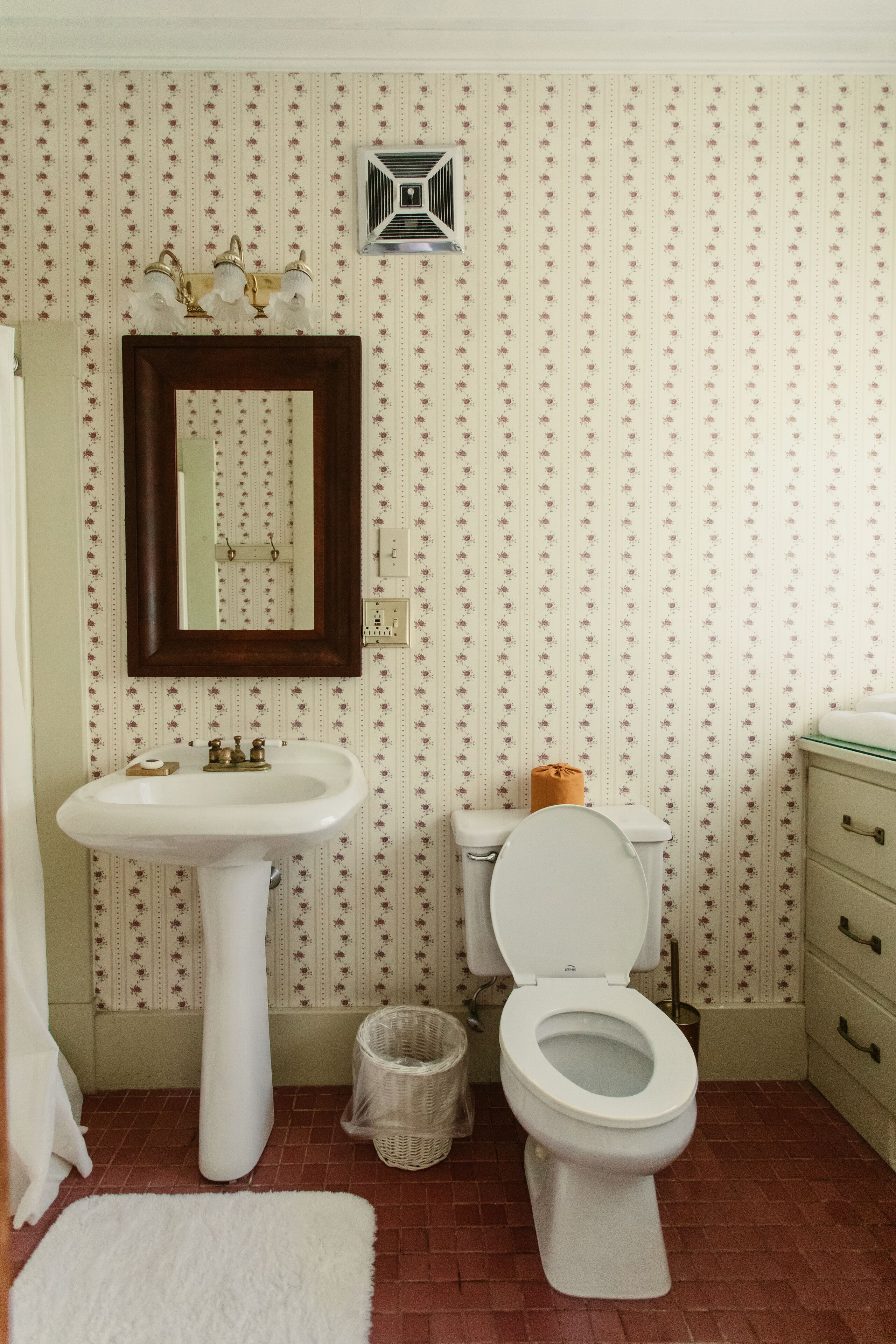 A bathroom with a white sink, a toilet, a mirror, and a patterned wallpaper.