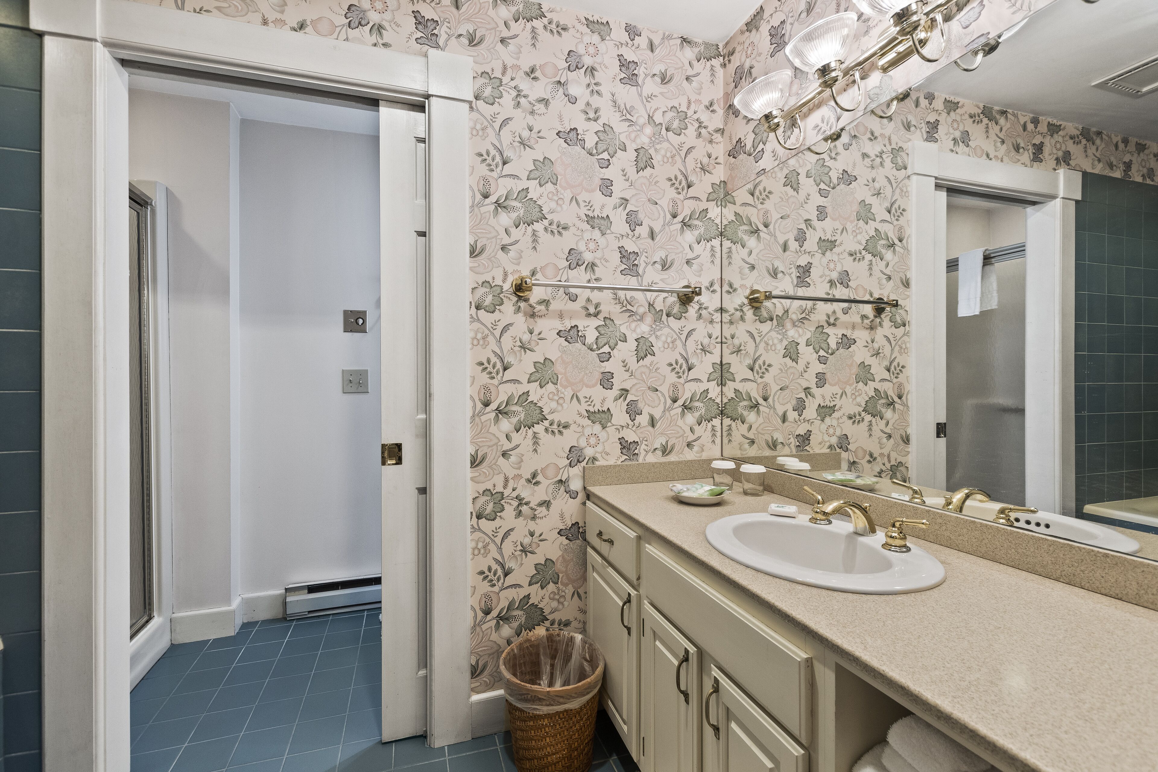 A bathroom with a floral wallpaper, a sink with a mirror, and a towel rack.
