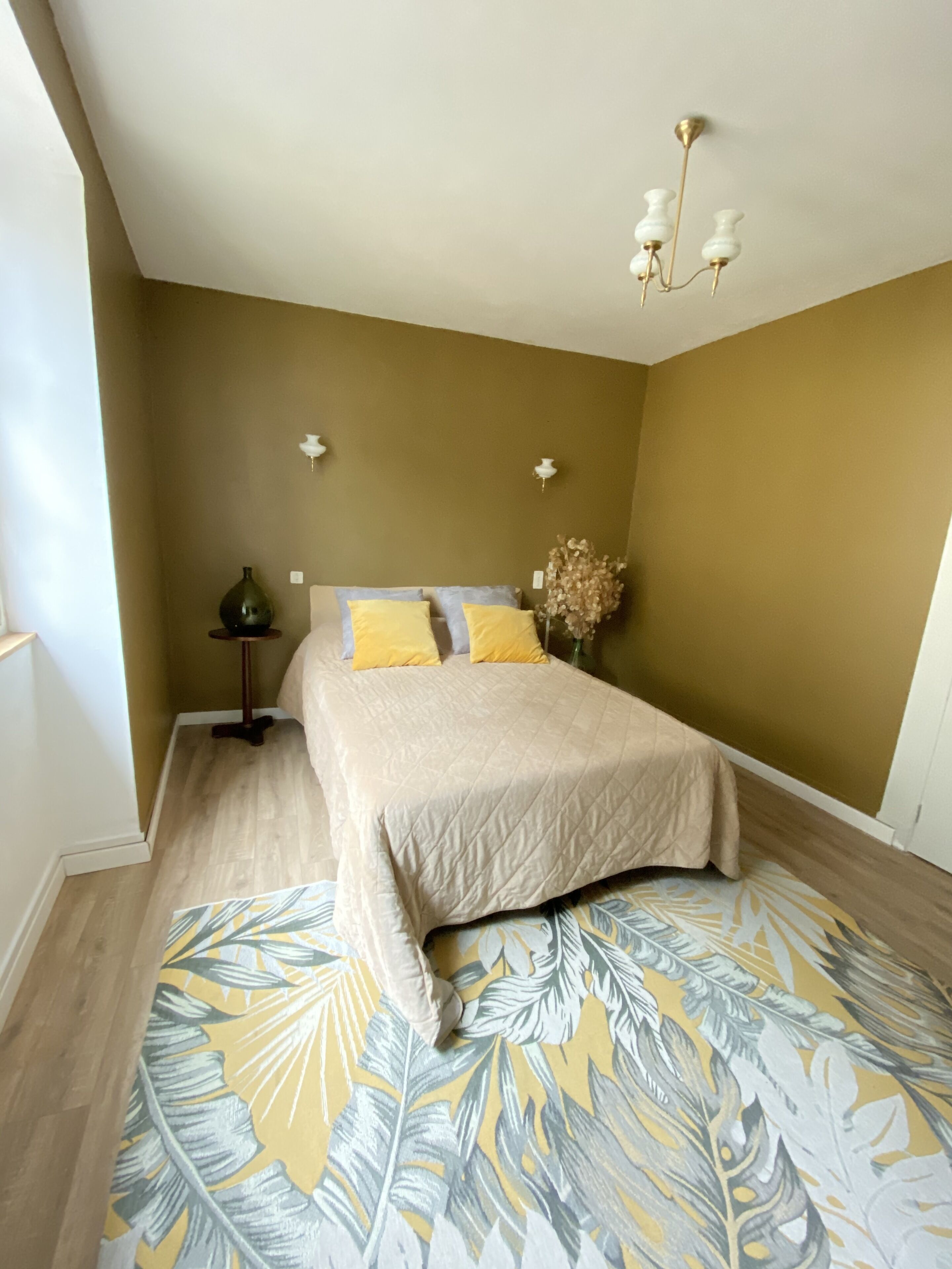 A bedroom with a bed, a nightstand, a vase with flowers, and a ceiling light fixture.