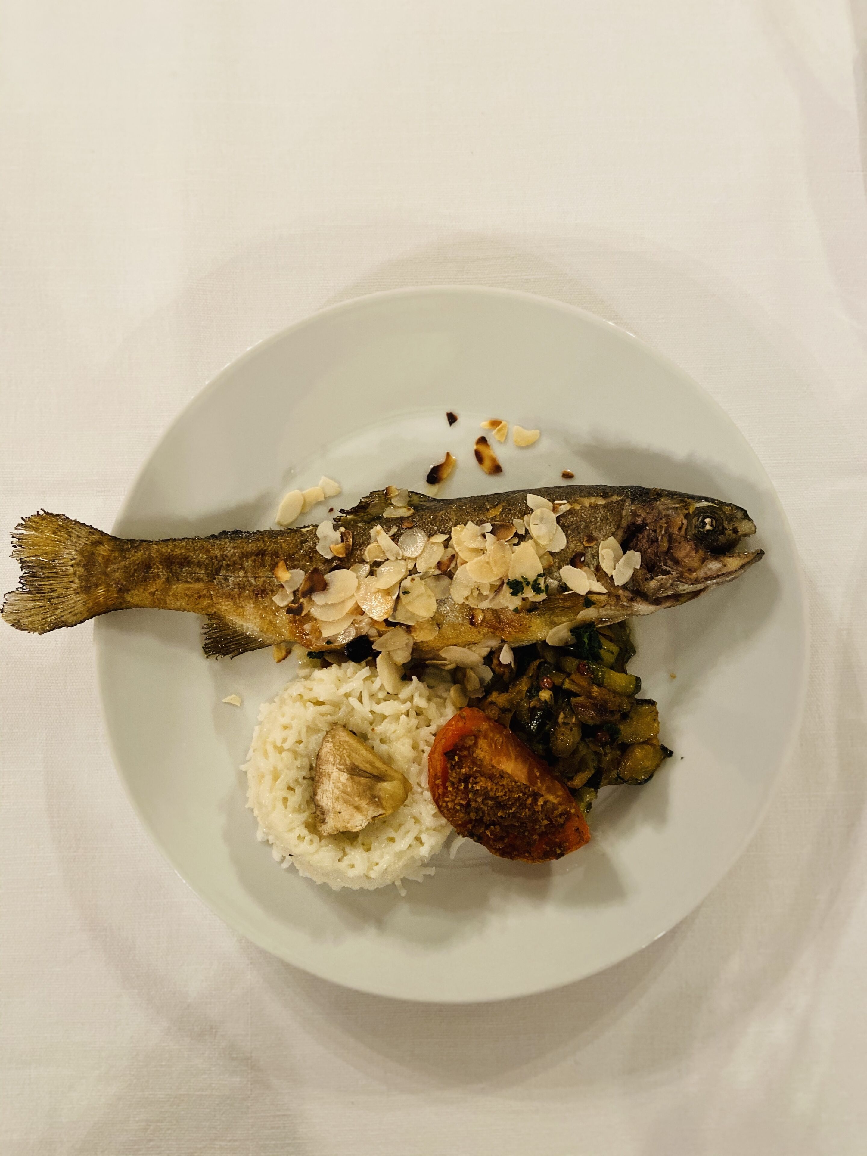 Un plato con un pescado entero, arroz y una rodaja de tomate.