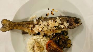 Un plato con un pescado entero, arroz y una rodaja de tomate.