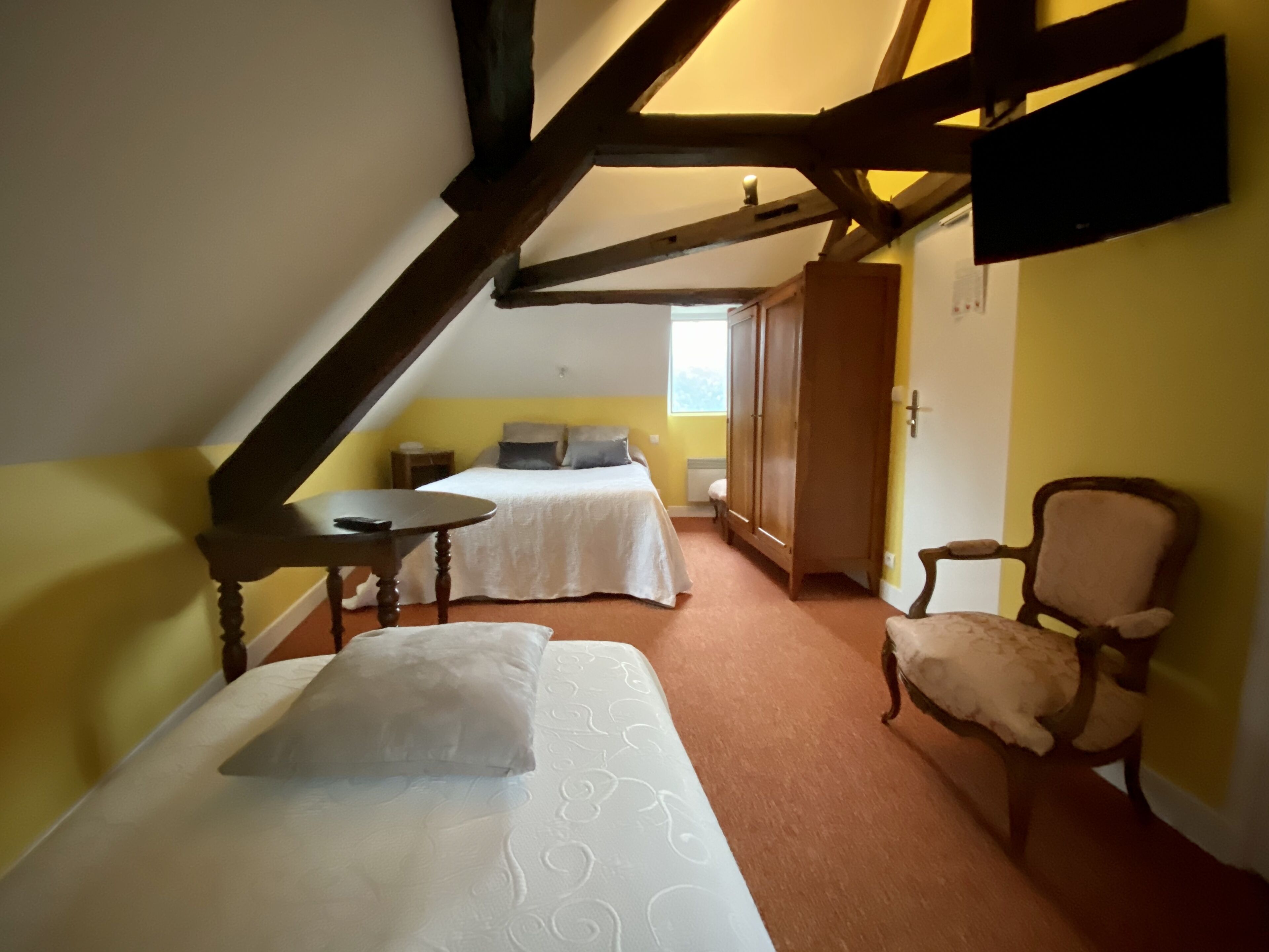 A room with two beds, a small table, a chair, and a television mounted on the wall.
