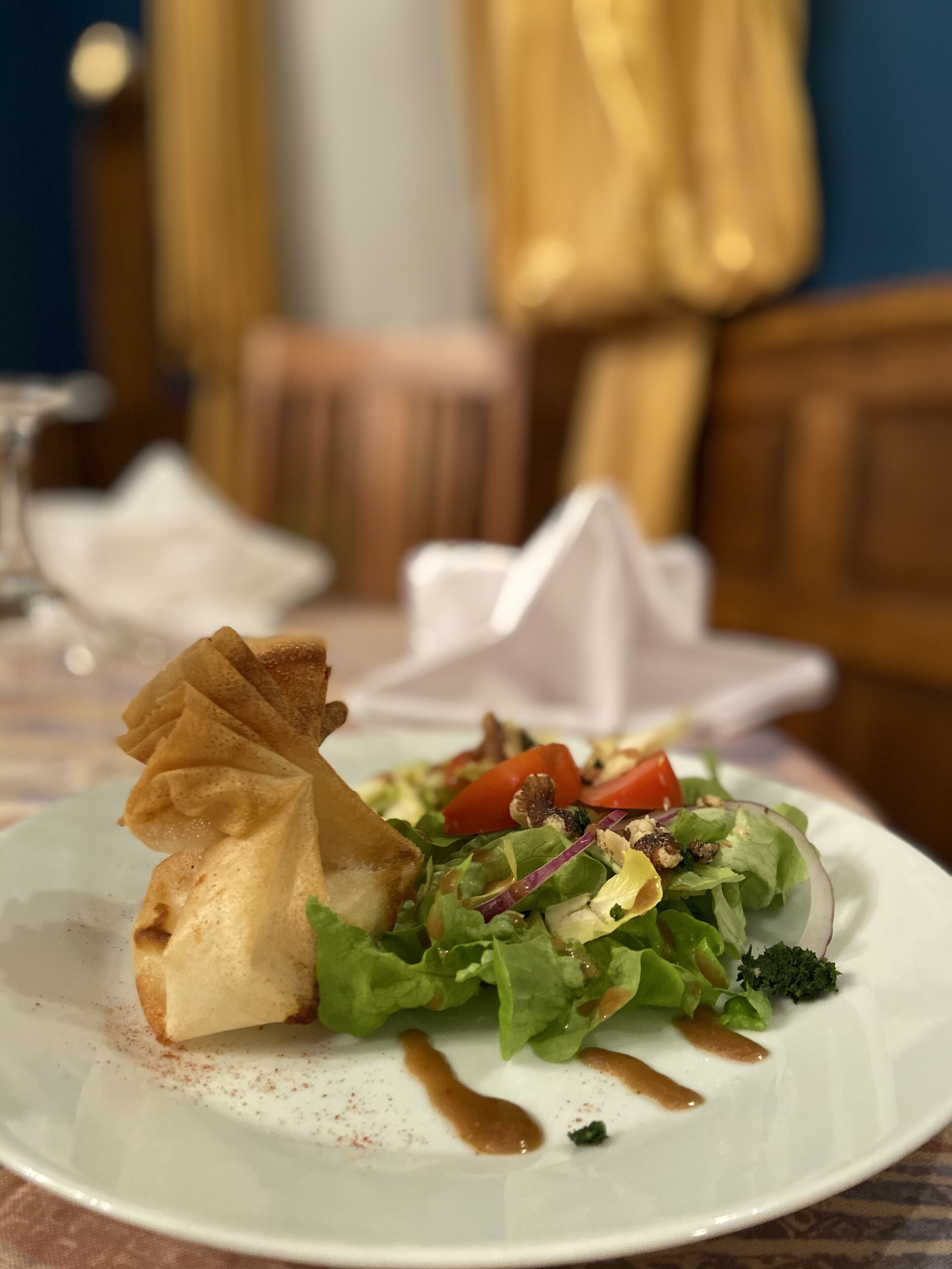 Un piatto di cibo con un'insalata e un dolce, su un tavolo con un tovagliolo bianco e un bicchiere d'acqua.