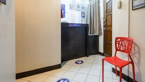 Un pasillo de hotel con una silla roja, un mostrador negro y señales de seguridad en el suelo.