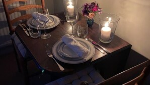 Una mesa de comedor para dos, con velas, un florero y una silla cómoda con cojín.