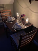 Una mesa de comedor para dos, con velas, un florero y una silla cómoda con cojín.