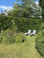 Un jardín con dos sillones de descanso y un seto.