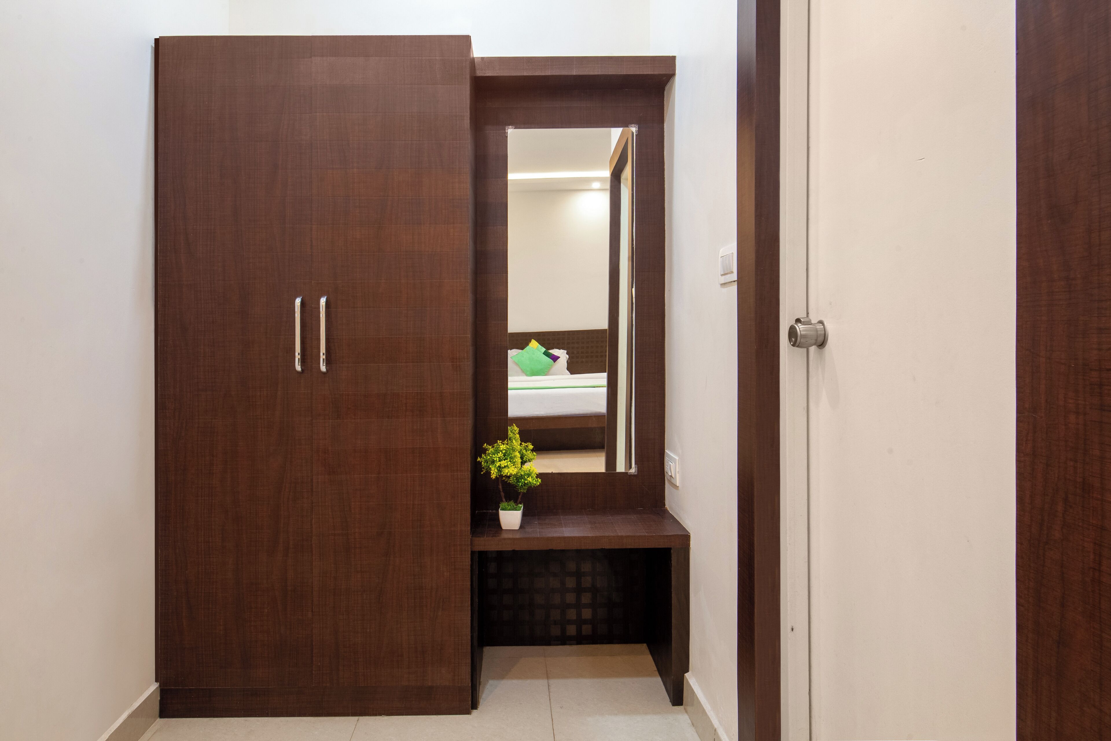 Un placard en bois avec un miroir, un petit banc et une plante en pot, le tout placé dans un couloir.