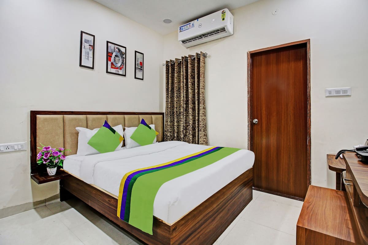 A neatly made bed with a wooden headboard, a bedside table with a vase of flowers, and a wooden desk with a telephone.