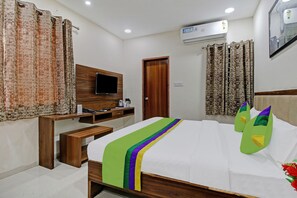 A hotel room with a bed, a TV, a wooden desk, a chair, a bench, and a door. - Treebo Krishna Regency ISBT Bus Stop (Bhopal)