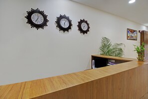 A reception area with a wooden counter, three wall clocks, and two potted plants.