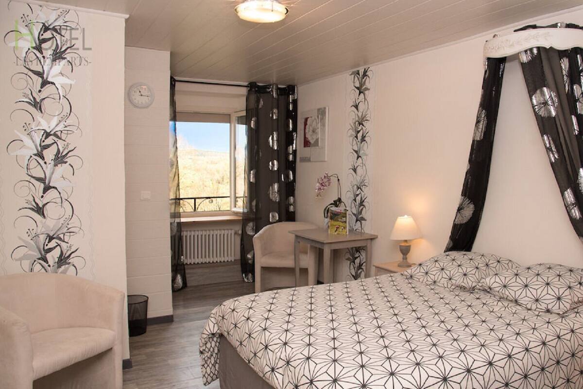 Ein Hotelzimmer mit Bett, Stuhl, Tisch mit Lampe und Blick ins Freie.