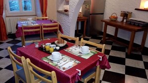 Un coin repas avec un sol à carreaux, des chaises en bois et des tables dressées avec des aliments pour le petit-déjeuner.