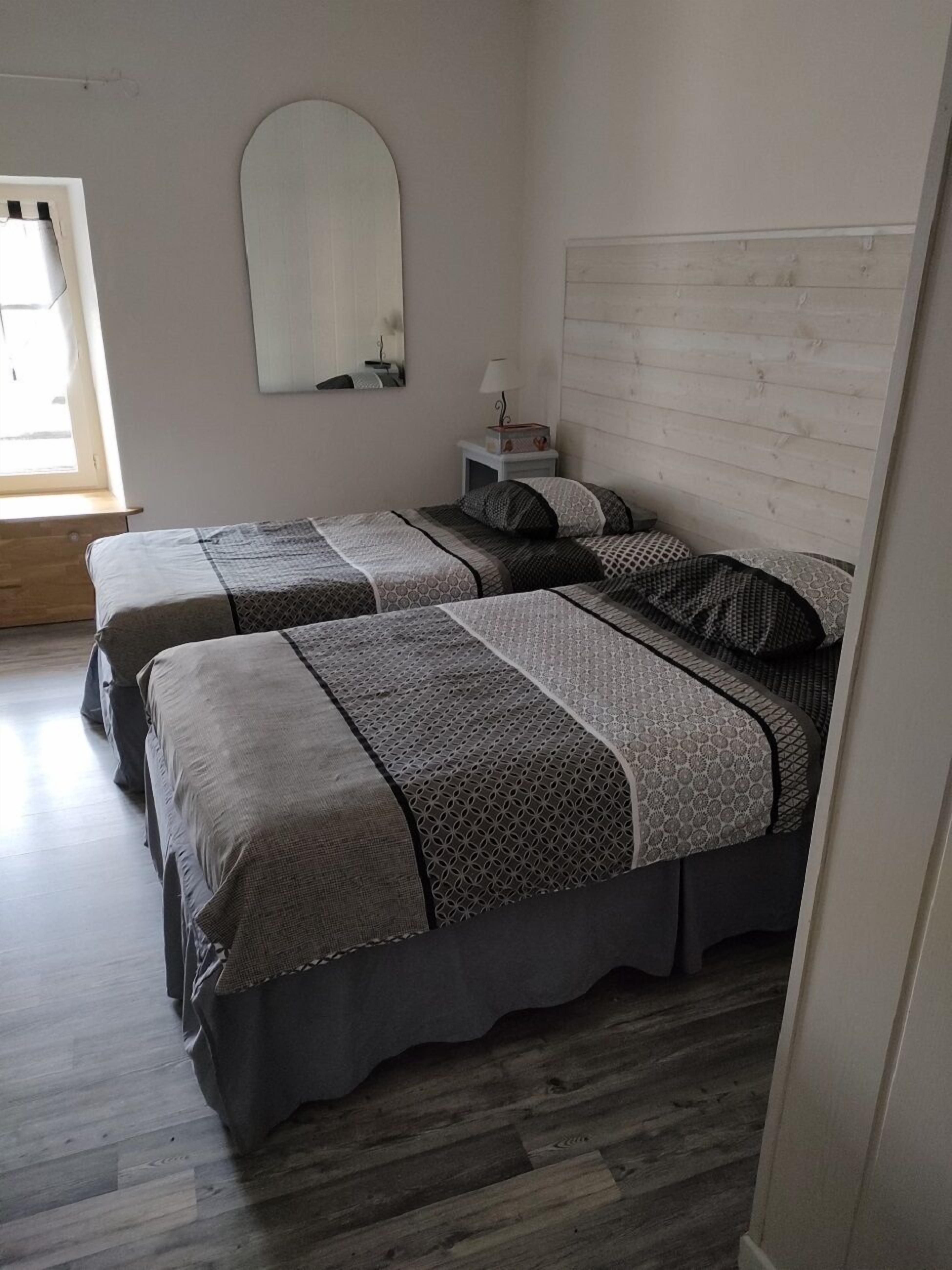 A room with two beds, a mirror, a nightstand, and a window.