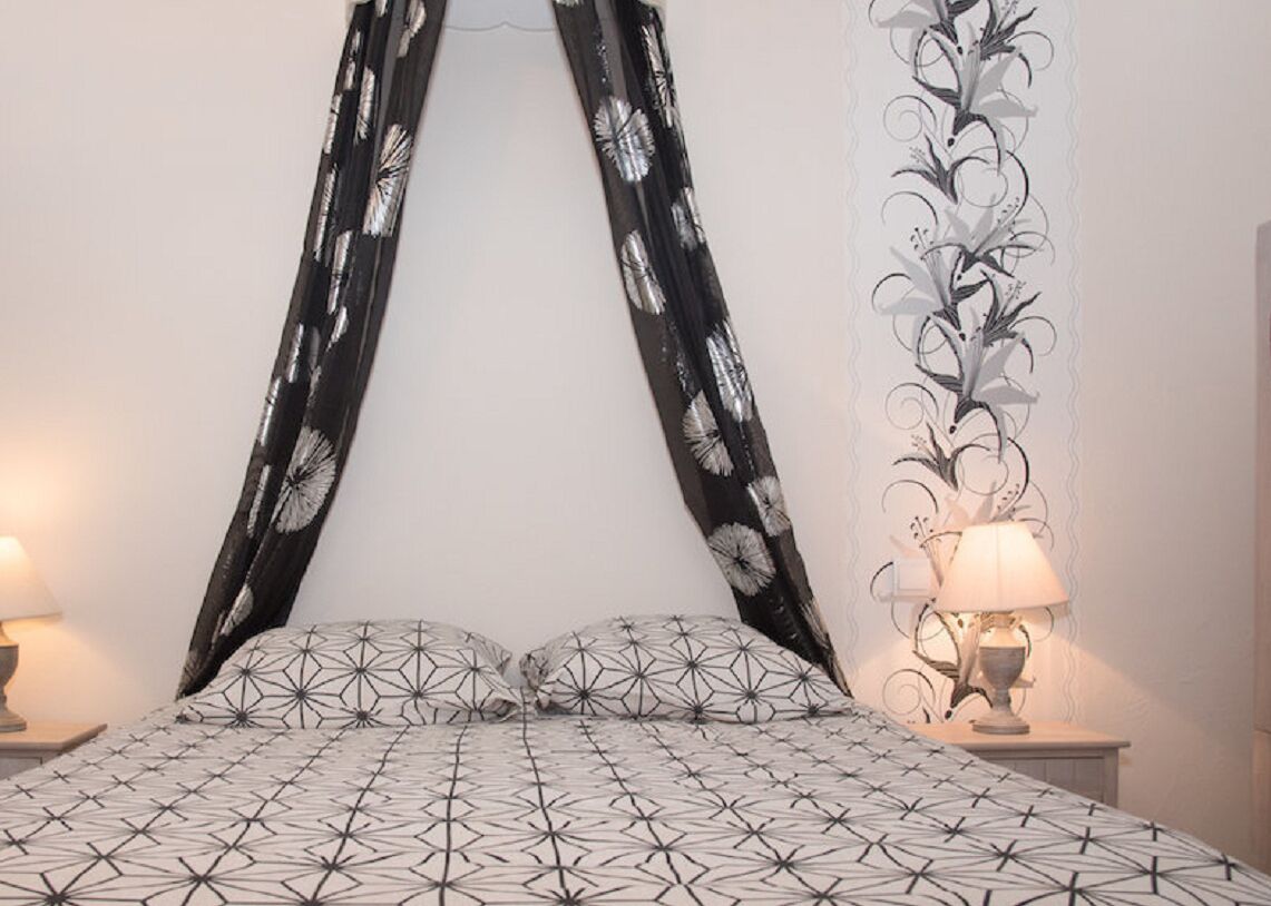 A bedroom with a geometric patterned bedspread, a canopy with a black and white floral design, and a wall with a white floral wallpaper.