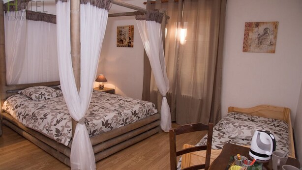 Une chambre avec deux lits, chacun doté d’un baldaquin, d’une tête de lit en bois et d’une couvre-lit à motifs floraux. On y trouve une petite table avec une bouilloire, des tasses et un chapeau.