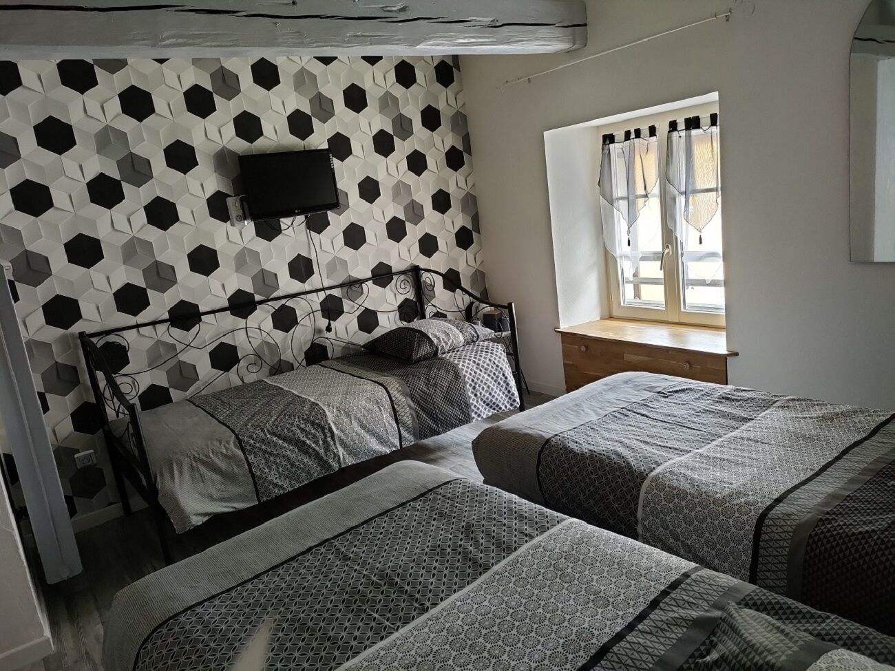 A room with two beds, a TV on the wall, and a window with curtains.