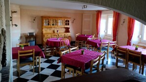 Un espace repas avec un sol à carreaux, des tables en bois recouvertes de nappes violettes et un buffet en bois à l’arrière-plan.