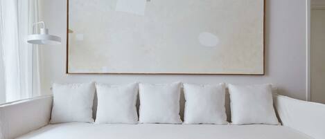 A white sofa with five cushions, a white wall, and a large abstract painting.