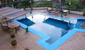 Una piscina en la azotea con borde azul, rodeada de mobiliario exterior y plantas en macetas.