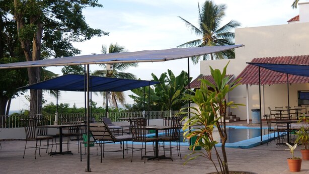 Área de estar externa com mesas, cadeiras, piscina e vasos de plantas.
