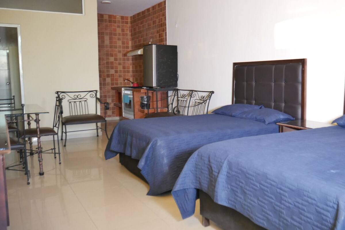 Een hotelkamer met twee bedden, een kitchenette, een eethoek met stoelen en een televisie.