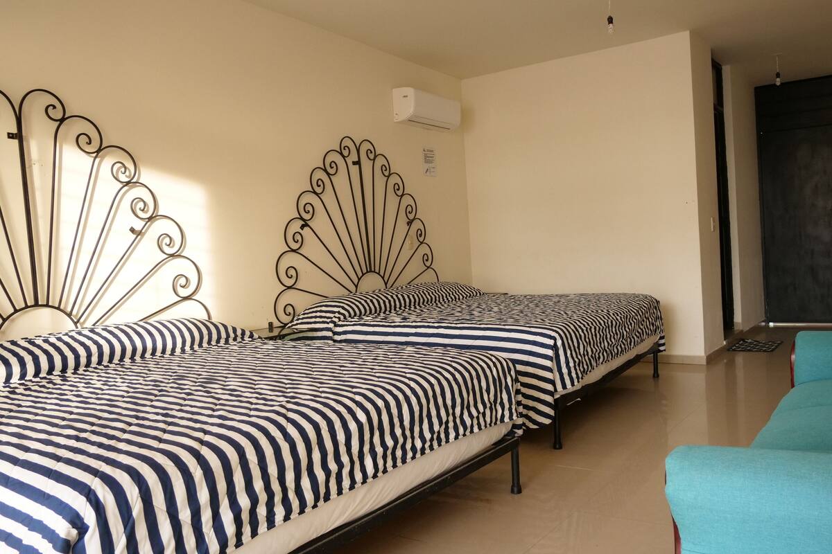 Een kamer met twee bedden met streepjesbeddengoed, een blauwgroene fauteuil en een schoolbord aan de muur.