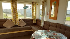 Una habitación acogedora con un sofá marrón, una mesa redonda con mantel estampado y una ventana con cortinas.