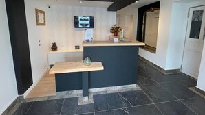 A reception area with a modern design, featuring a reception desk, a mounted television, and a small plant. - Le Central Hôtel Bar (Oloron-Sainte-Marie)
