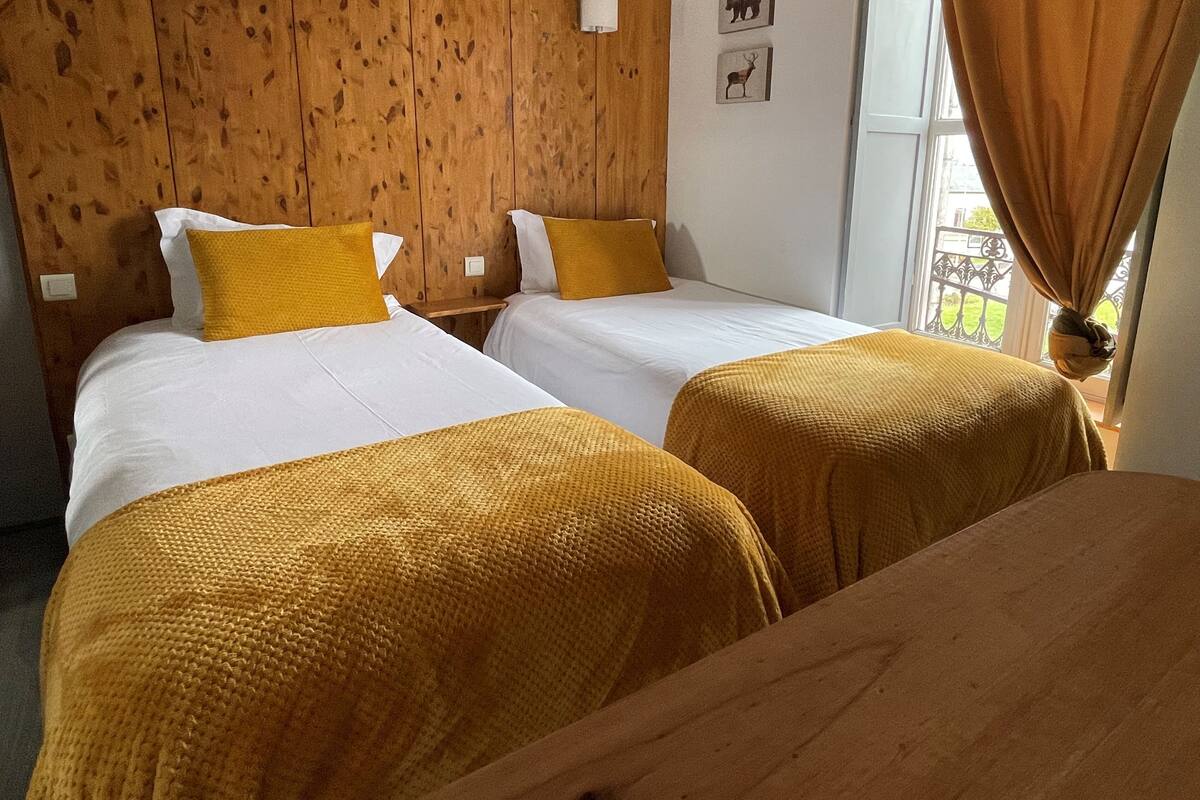 Une chambre d’hôtel avec deux lits, une tête de lit en bois, du linge de lit blanc et une fenêtre avec des rideaux.