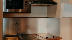 A compact kitchen with a stainless steel microwave, a sink, and a built-in oven. - Le Central Hôtel Bar (Oloron-Sainte-Marie)
