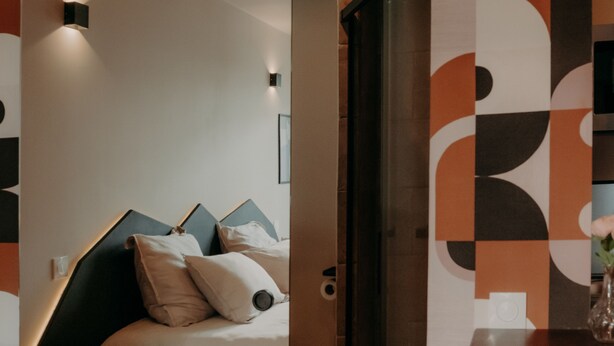 A modern hotel room with a bed, bedside table, and a patterned wall. - Le Central Hôtel Bar (Oloron-Sainte-Marie)