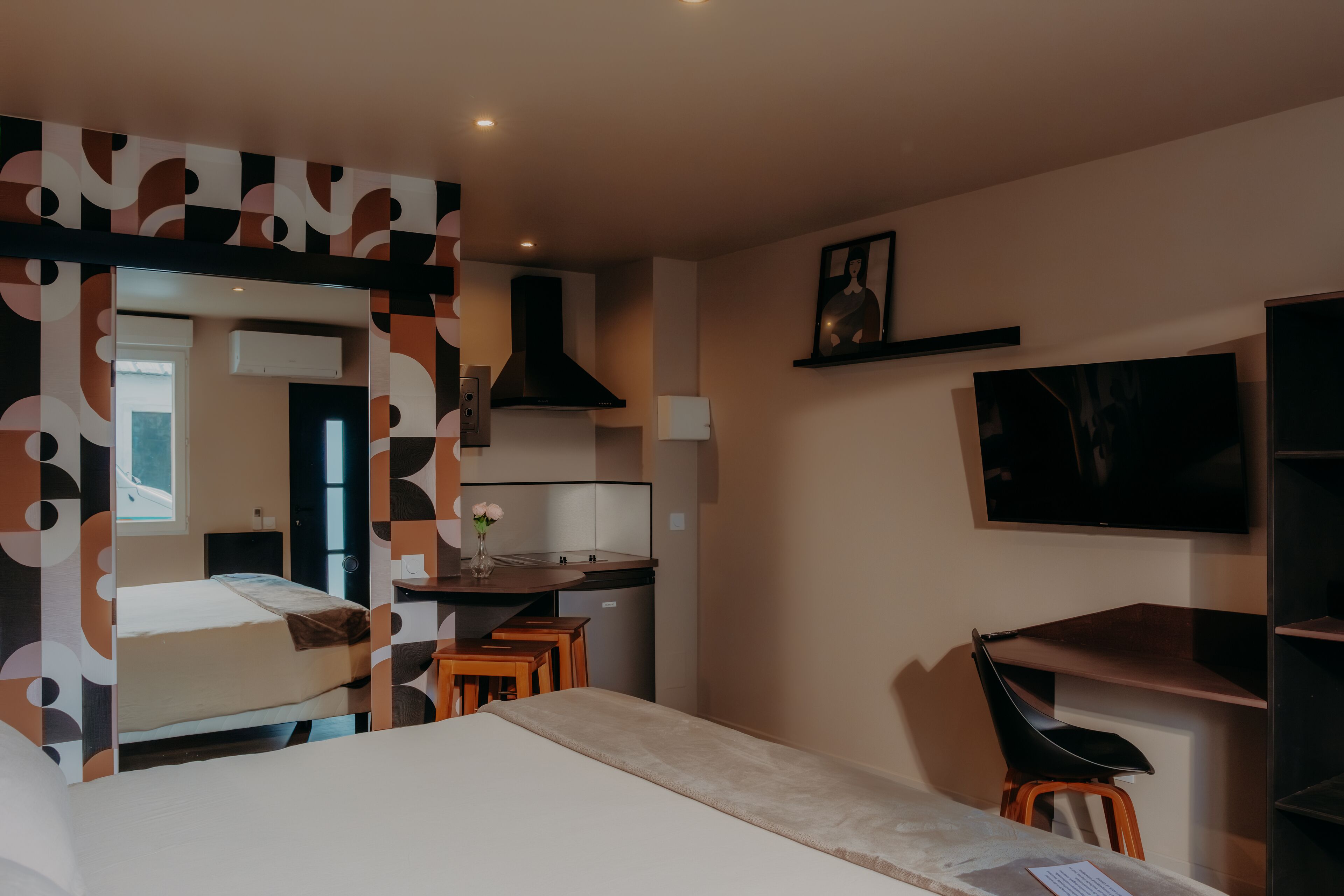 Een kleine hotelkamer met een bed, bureau, stoel, televisie en kitchenette.