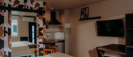Una habitación de hotel pequeña con cama, escritorio, silla, televisor y kitchenette.