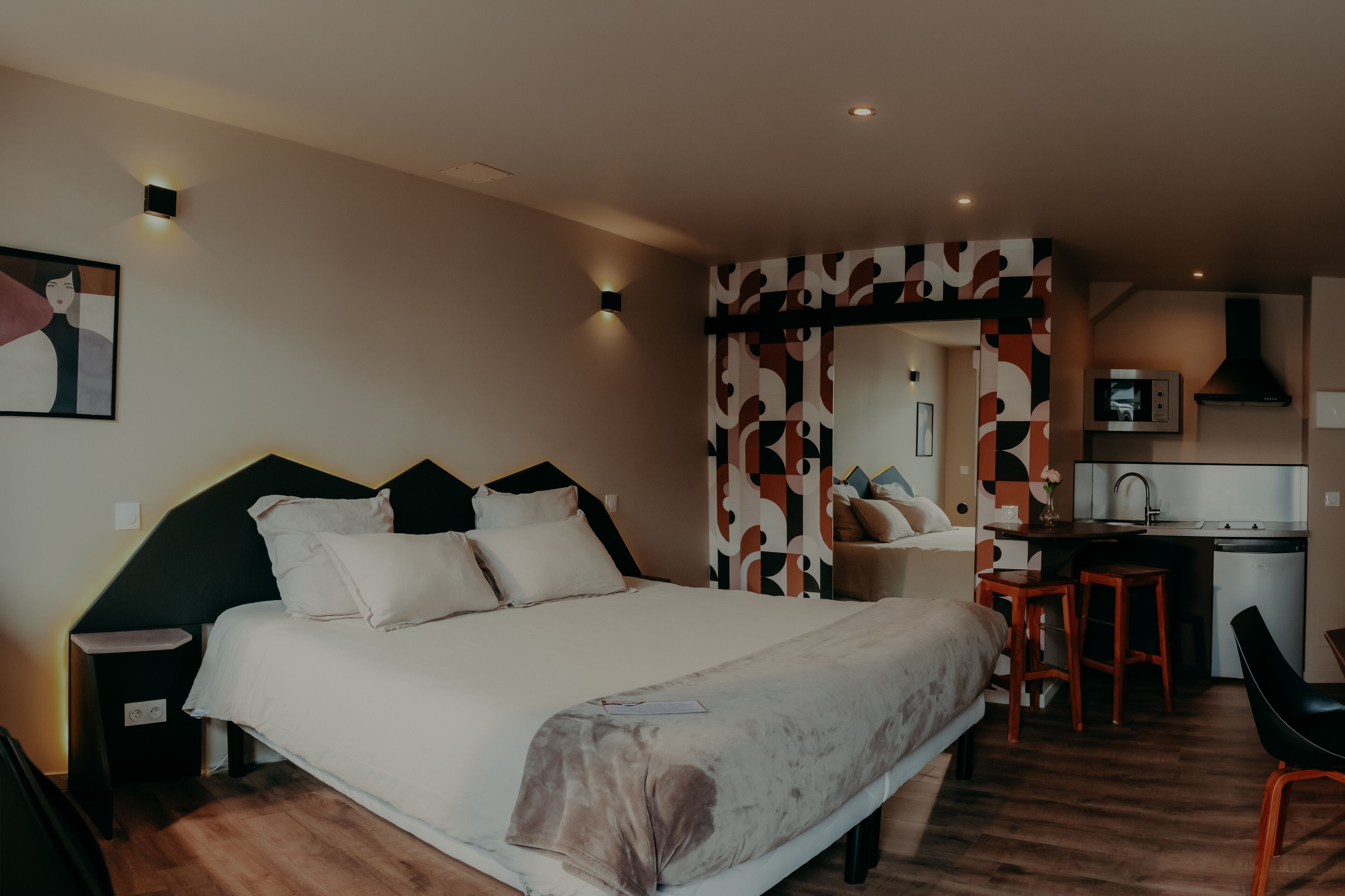 Un dormitorio con cama, mesitas de noche, un escritorio y una kitchenette.