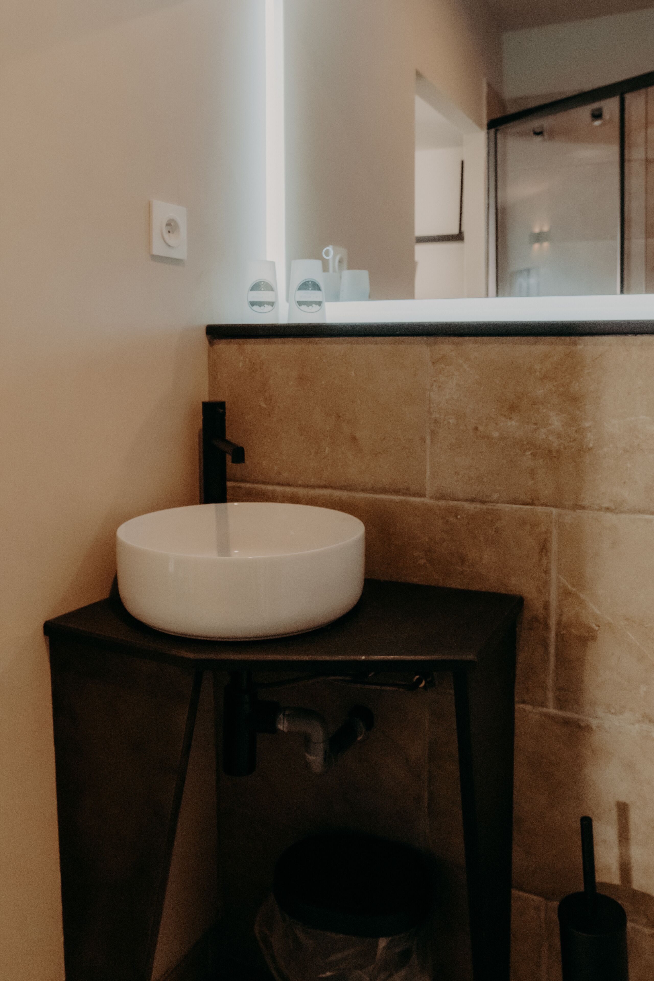 Une salle de bain avec un lavabo blanc, un robinet noir et une poubelle.