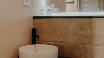 Une salle de bain avec un lavabo blanc, un robinet noir et une poubelle.