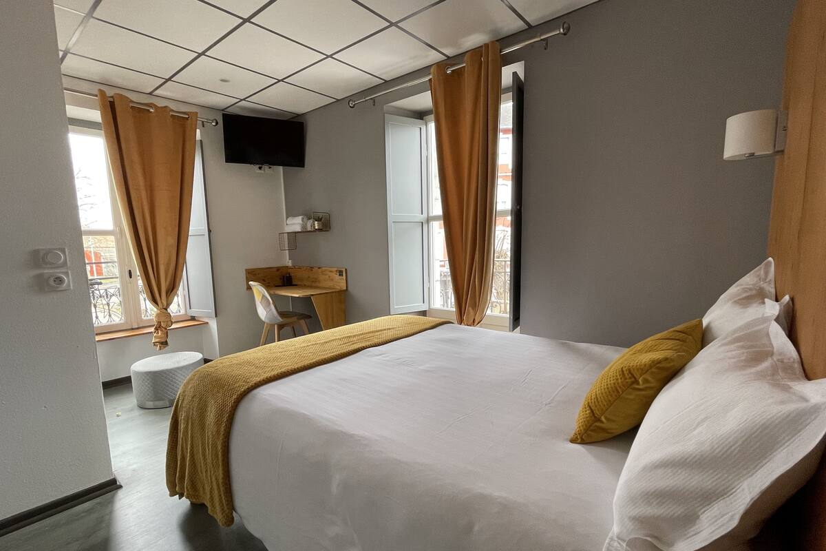 Une chambre d’hôtel équipée d’un lit, d’un bureau, d’une chaise, d’une télévision et d’une fenêtre avec des rideaux.