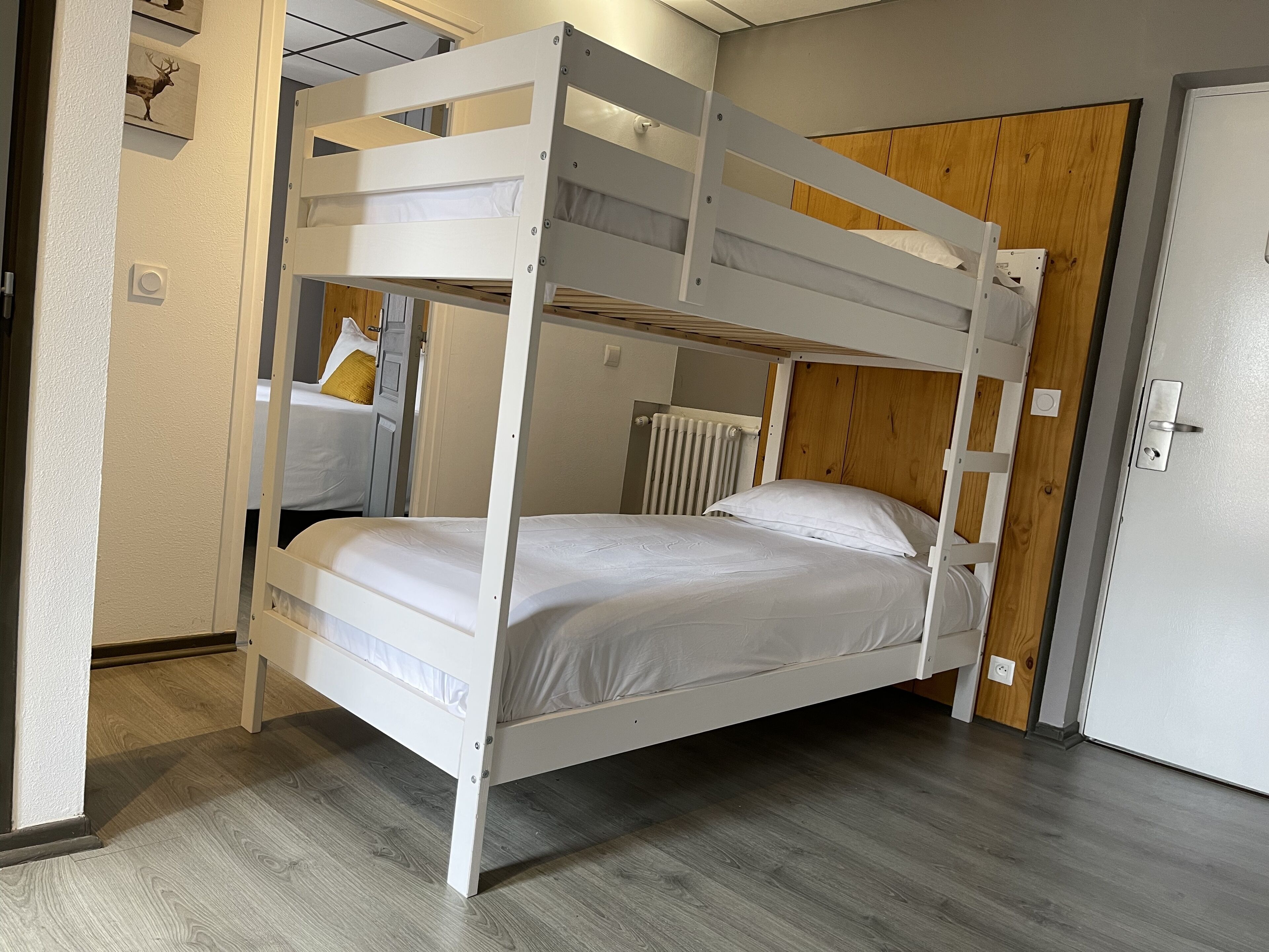 A bunk bed with white bedding, a wooden door, and a radiator.