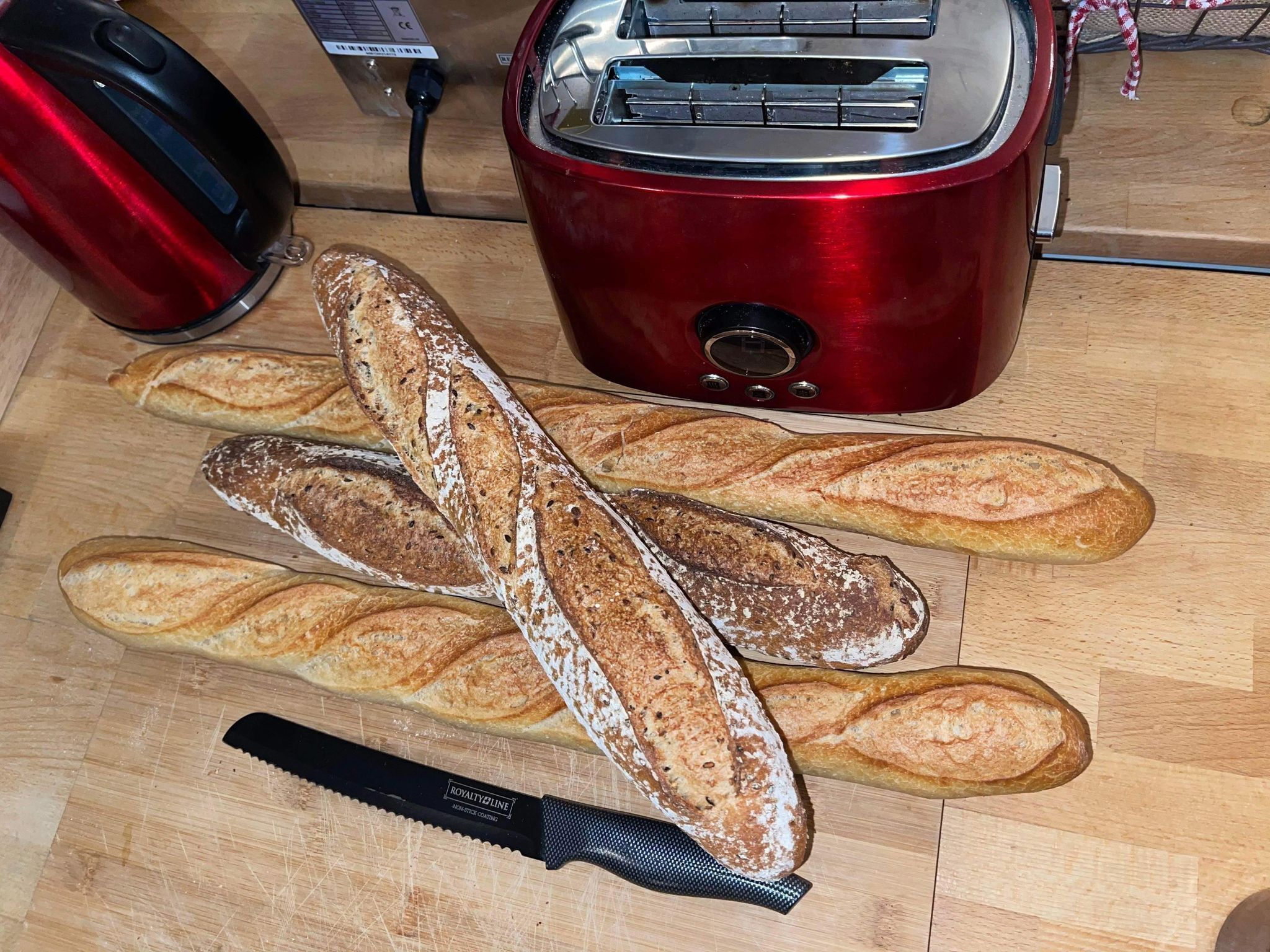 A wooden cutting board with several loaves of bread and a knife.