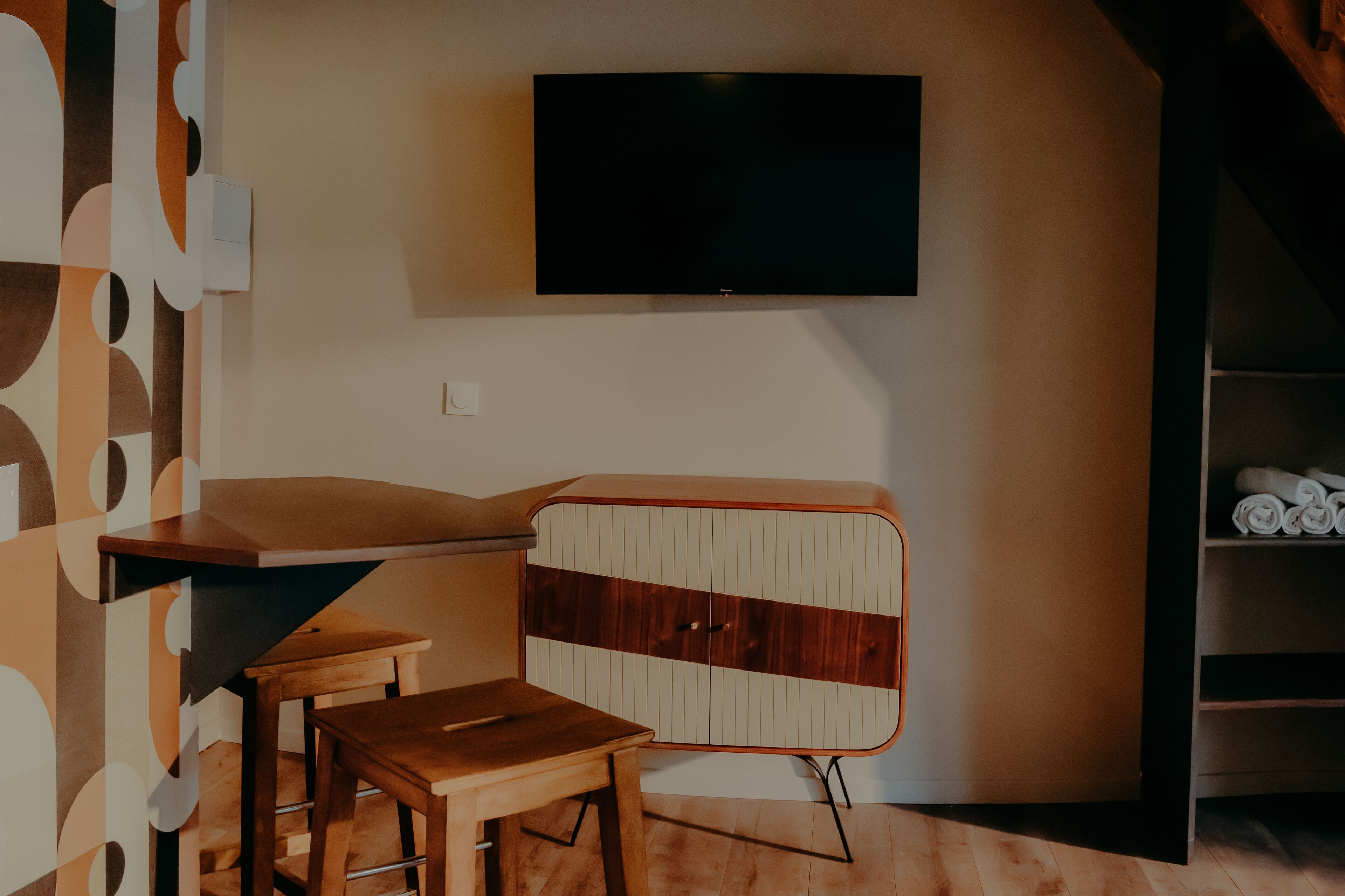 A modern room with a flat-screen TV mounted on the wall, a wooden table, and a cabinet with a striped design.