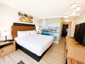 Habitación de hotel con una cama grande, un escritorio con televisor, un cuadro en la pared y vistas a un puente.