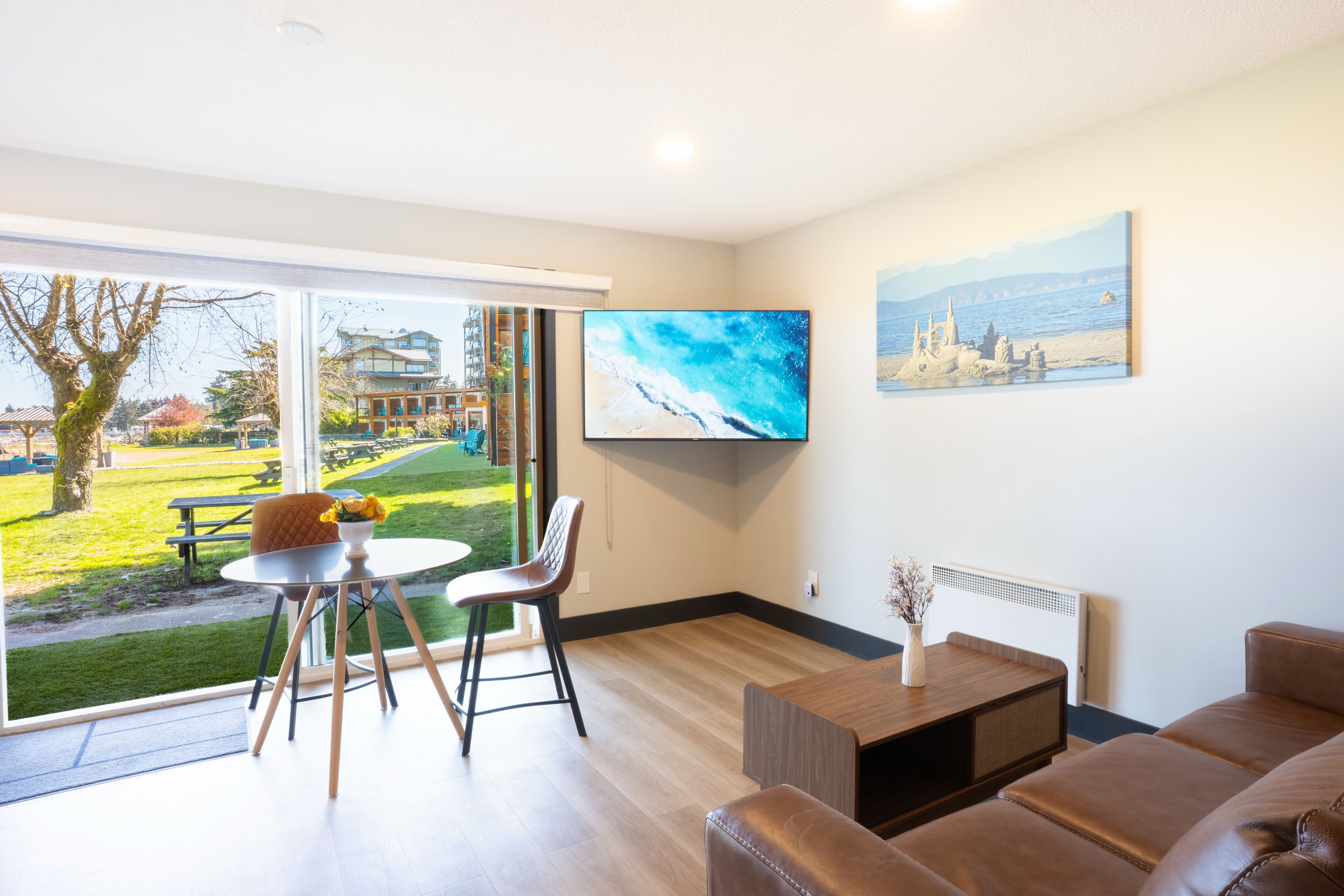 A modern living room with a large window, a flat-screen TV, and a view of a park and buildings outside.