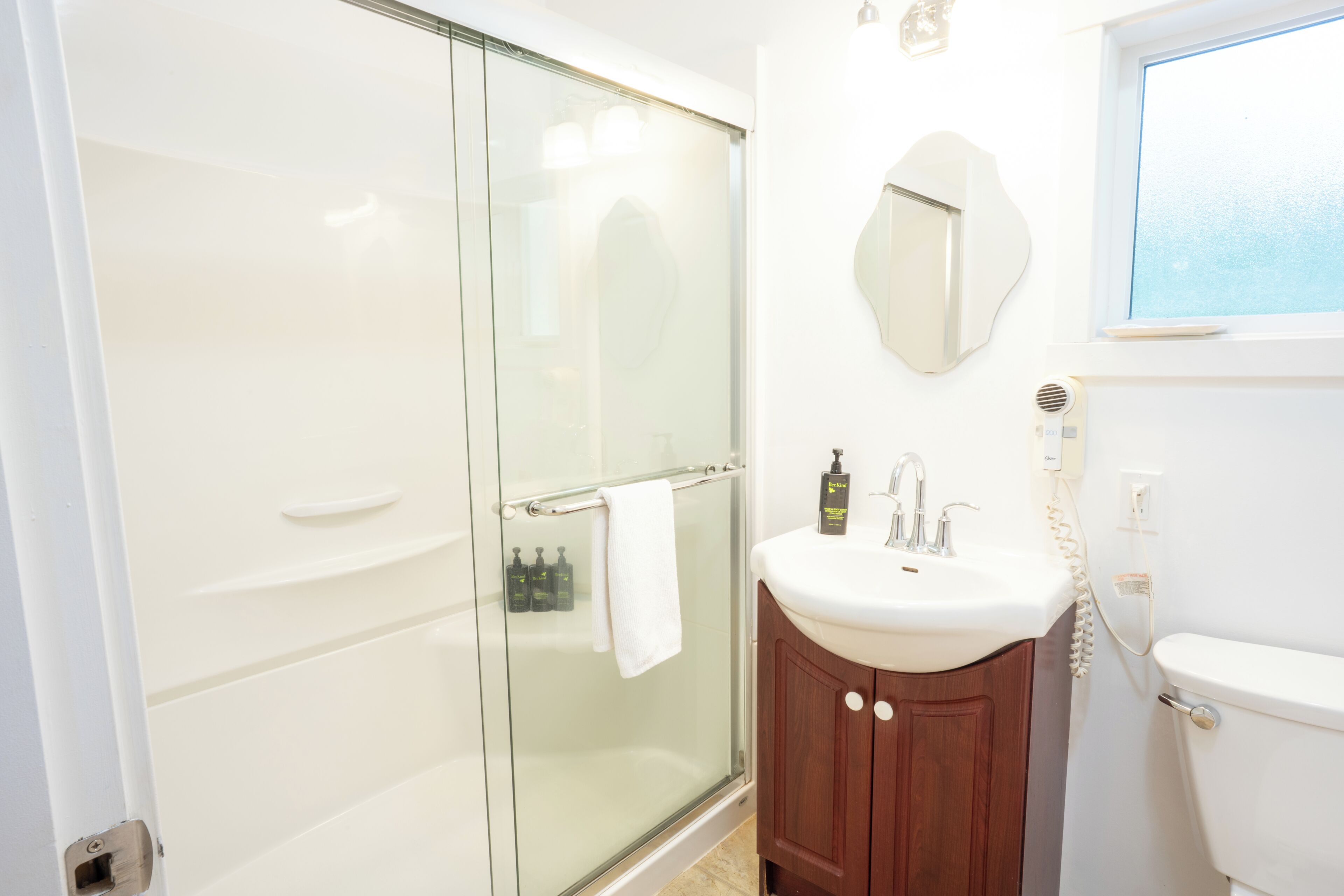 A bathroom with a glass shower enclosure, a white sink, a wooden cabinet, a mirror, and a toilet.