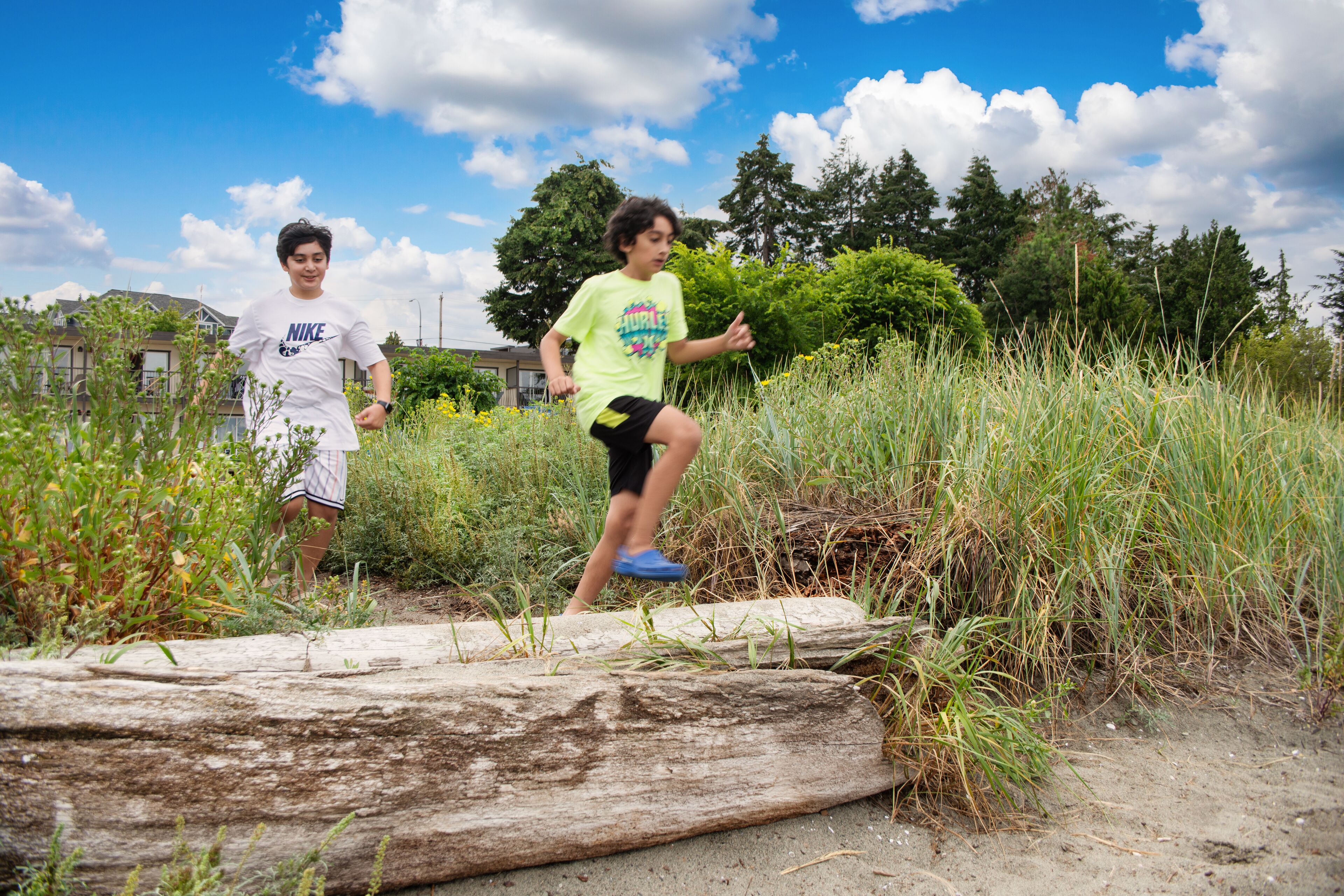 Two people walking on a dirt path with grass and trees in the background.
