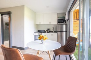 Cocina moderna con armarios blancos, electrodomésticos de acero inoxidable y una zona de comedor con una mesa blanca y dos sillas.
