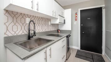 Una cocina moderna con armarios blancos, un lavamanos de acero inoxidable y un microondas integrado.